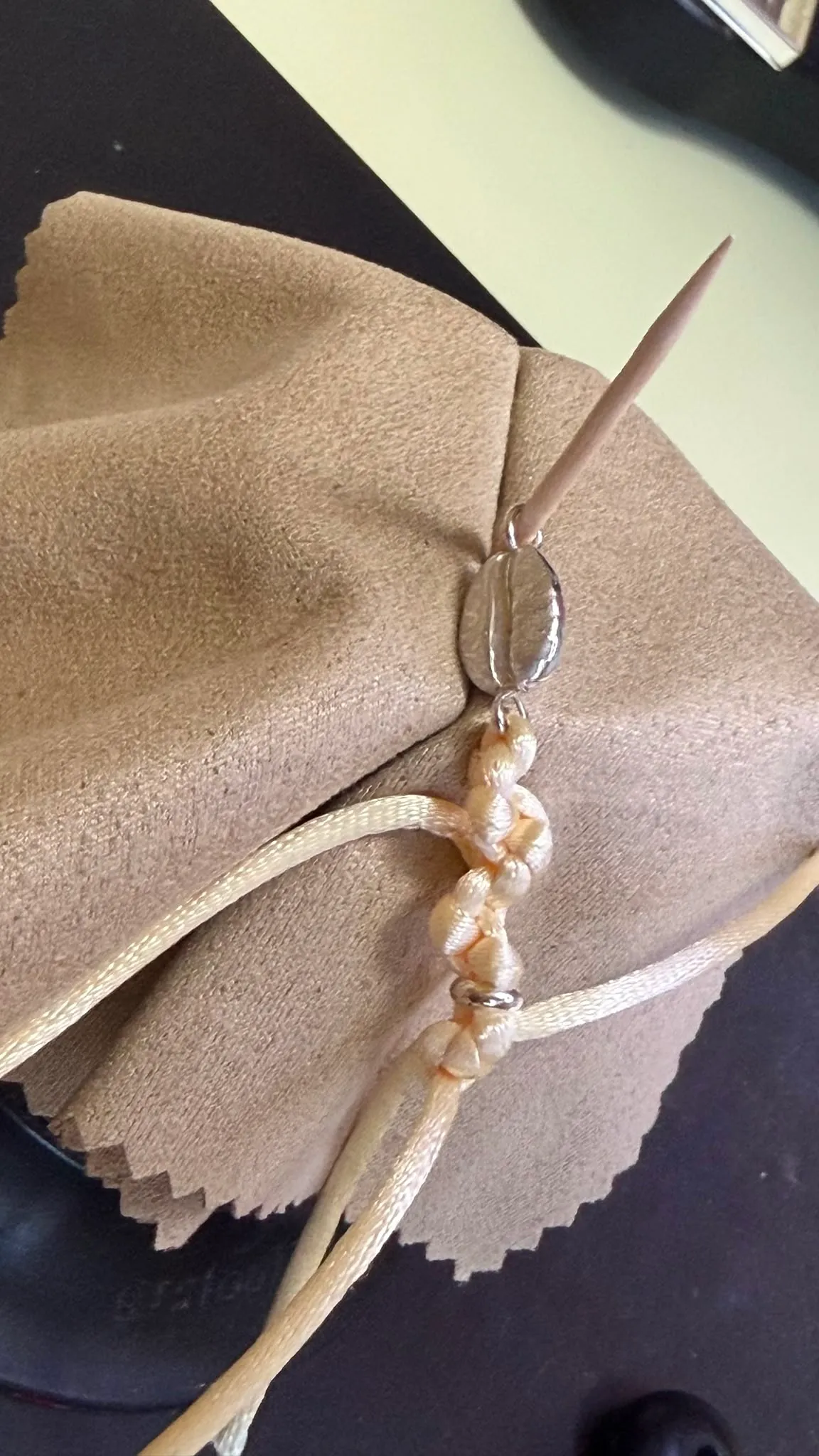 Le grain d'argent et son cordon noué, posés sur la pochette de l'atelier.