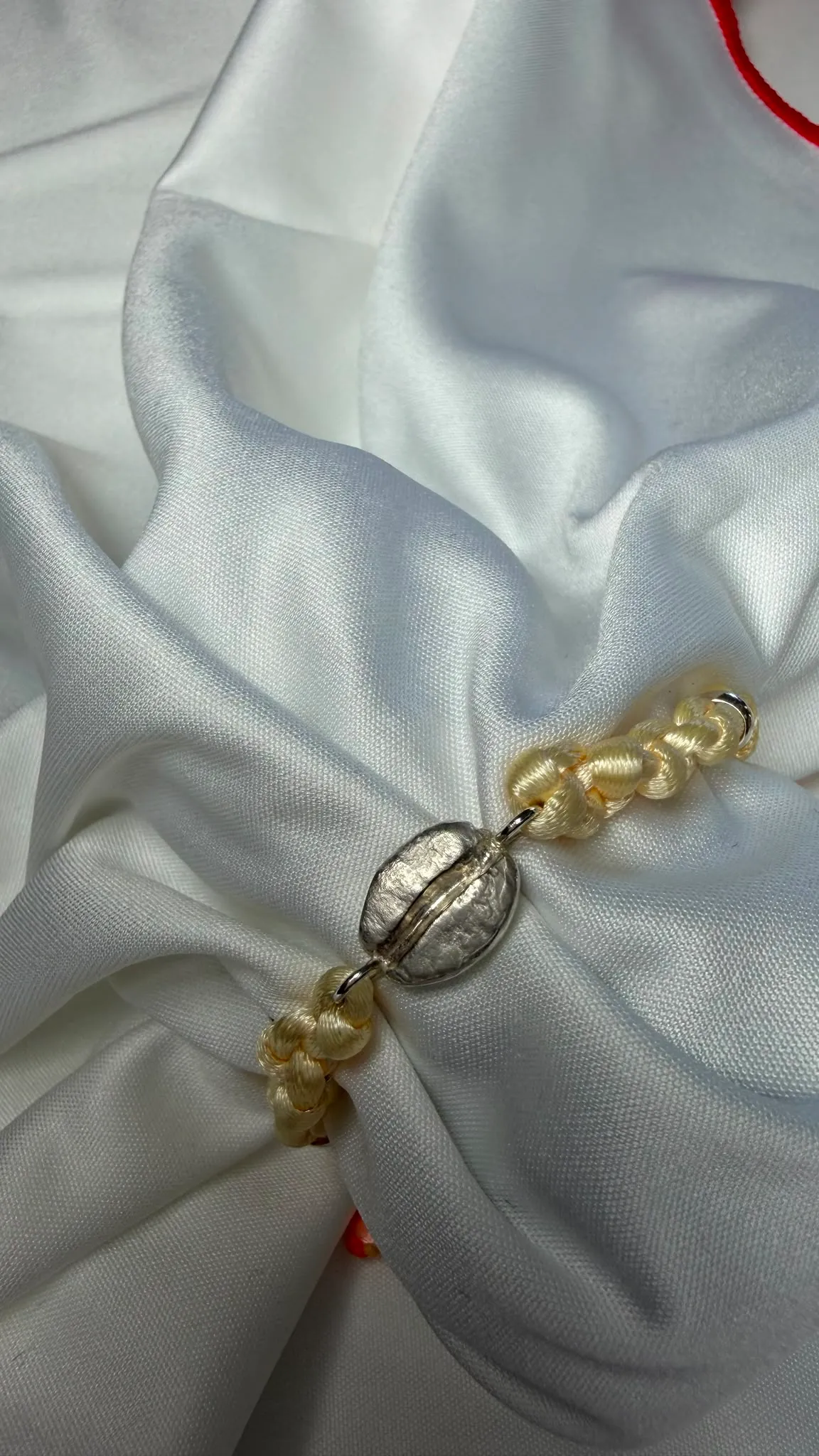 Le bracelet « Le grain » posé sur la soie, le grain d'argent au centre, le cordon noué.