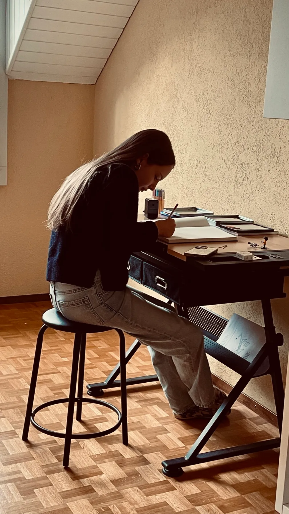 Une jeune personne assise à la table à dessin de l'atelier, en train de dessiner.