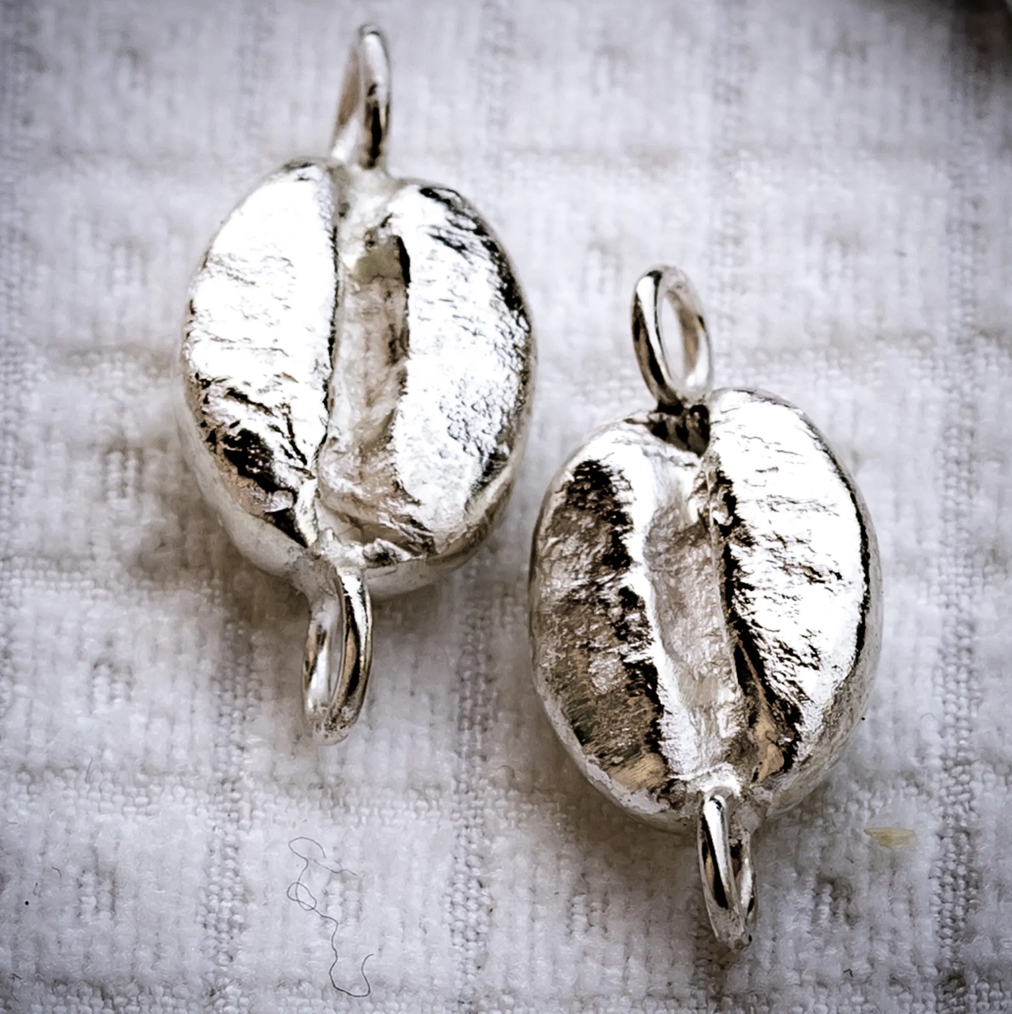 Deux grains d'argent à bélières, posés sur une toile écrue.